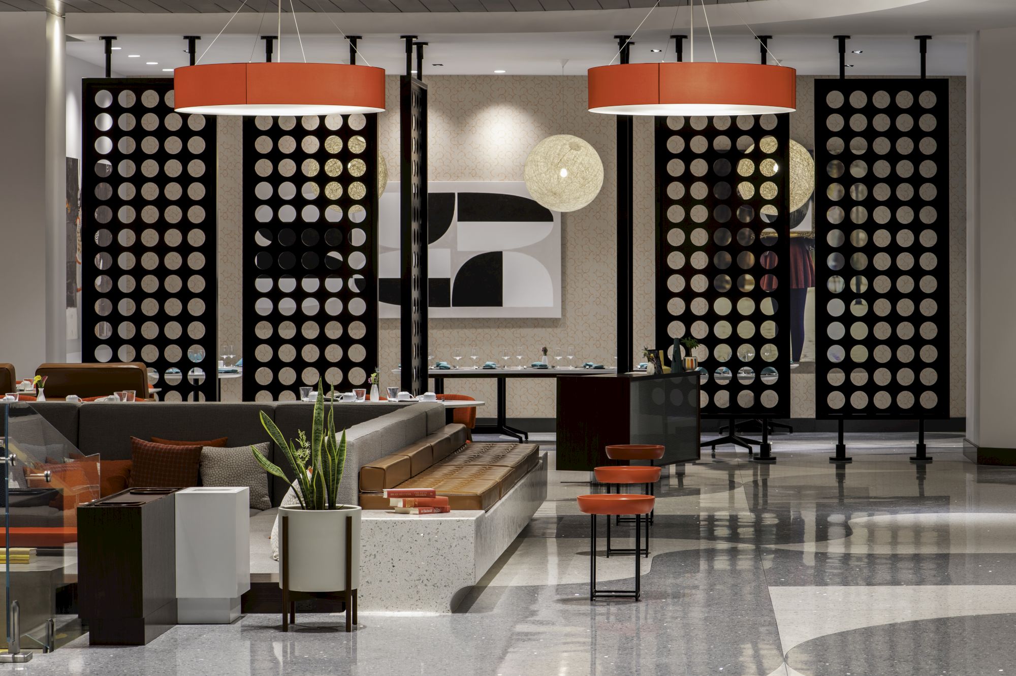 A modern lounge with red pendant lights, black panel walls covered in circular patterns, and a seating area with red stools.